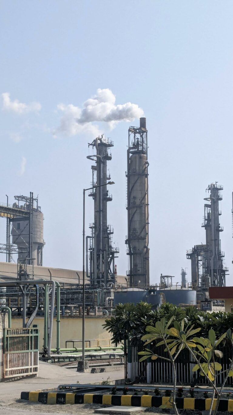 A detailed view of a chemical plant's tall chimneys and industrial structures against a clear sky.