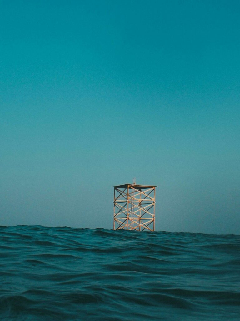 A solitary offshore platform surrounded by wavy ocean waters under a clear blue sky. Ideal for backgrounds.