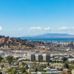 Aerial view of an urban area with an oil refinery by the sea and mountains.