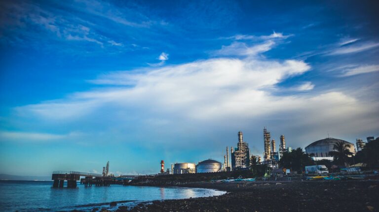 Industrial buildings by the sea under a dramatic cloudy sky.